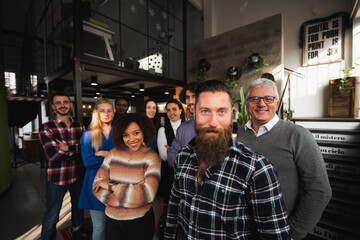 Portrait of casual and mixed trace group of colleagues in a modern office standing looking at camera smiling.