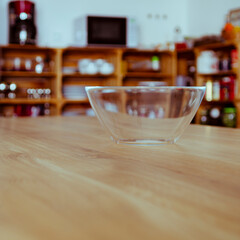 An empty glass bowl stands on a wooden table against a wooden kitchen background