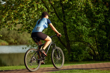 Naklejka premium Happy brunette girl in sportswear riding a bike in the park.