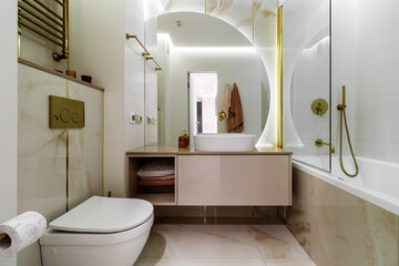 White marble bathroom with round mirror, gold faucets and shower