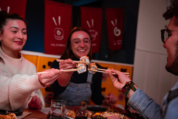 The group of friends from Europe use their chopsticks to bump their sushi pieces and celebrate.