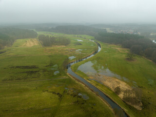 Blick auf einen kleinen geschlängelten Fluss von oben mit umgebender grüner Landschaft bei Nebel