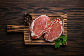 Cut raw meat pork steaks with seasonings on kitchen cutting board, rustic wooden background top...
