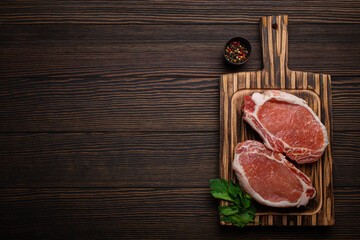 Cut raw meat pork steaks with seasonings on kitchen cutting board, rustic wooden background top view, ready for BBQ. Pork loin chops, space for text