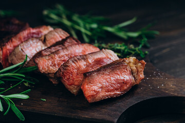 Grilled beef chuck roll steaks on wooden background with rosemary and thyme
