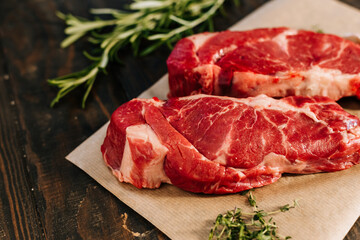 Raw chuck roll steaks on wooden background with rosemary and thyme close up