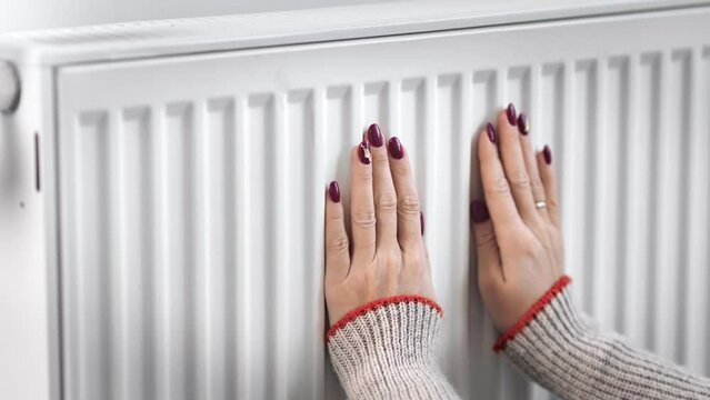 Home heating expensive cost European female hands touch hot thermostat radiator feeling cold winter