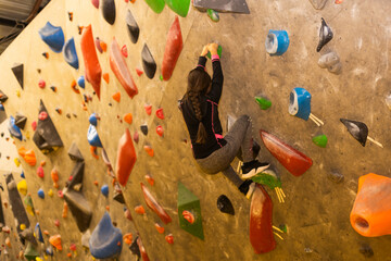Girl climbing on practical wall indoor, bouldering training