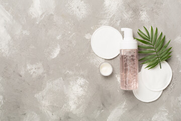 Foaming facial cleanser and with eco pads on concrete background, top view