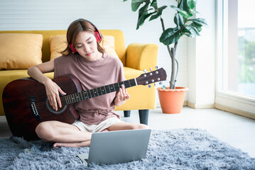 Asian woman attractive and young wearing headphones and learning to play guitar from online...