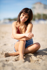 Fototapeta na wymiar Pretty young woman sitting on sandy beach on a summer day