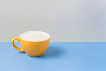 A yellow ceramic cup of coffee with steamed milk foam, cappuccino, latte, on blue beige background