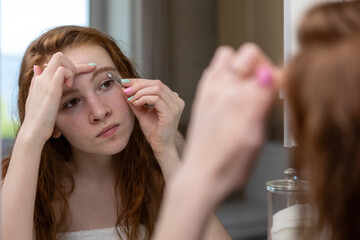 Teenage girl plucks her eyebrows looking in the mirror