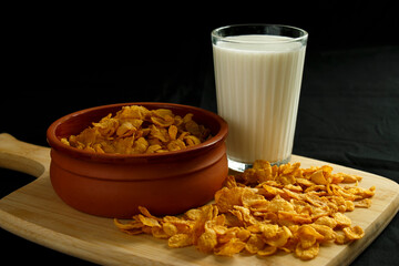 A bowl of cornflakes and a glass of milk on the kitchen board