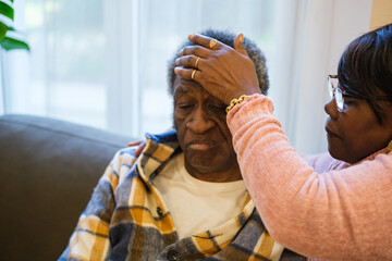 Senior woman taking the temperature with her hand of her partner who is ill with a fever. Concept: Health care, people care, retirement