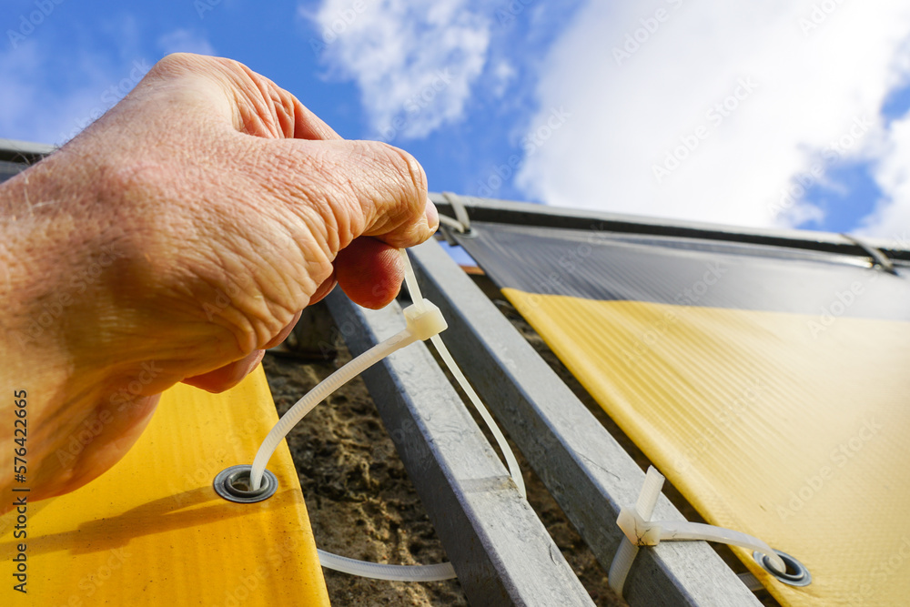 Wall mural fastening process of the outdoor ad banner to the metal frame with the help of plastic cable ties