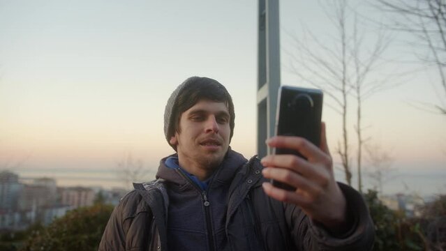 Young man having a video conference in the middle of nature at sunset, with his phone held horizontally