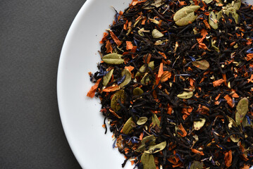 Black tea on a white plate. Dry tea with spices for brewing.