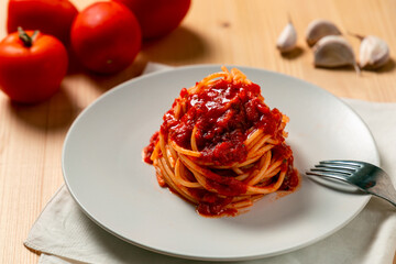 Spaghetti nest with tomato sauce over a wooden table, with a fork, kitchen towel, tomatoes and garlic