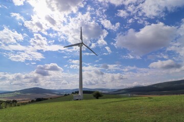 Obraz premium Wind power plant in landscape with turbine between the clouds at blue sky