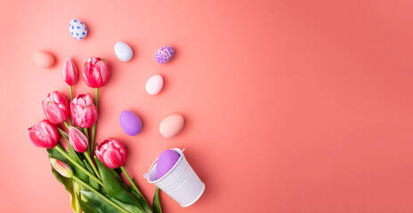 Colorful Easter eggs in decorative bucket and tulip flowers on pink background, flat lay. Space for text