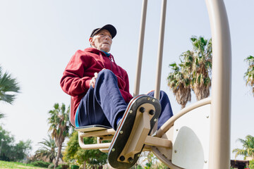 Frontal below view of an old man using a leg press in a park