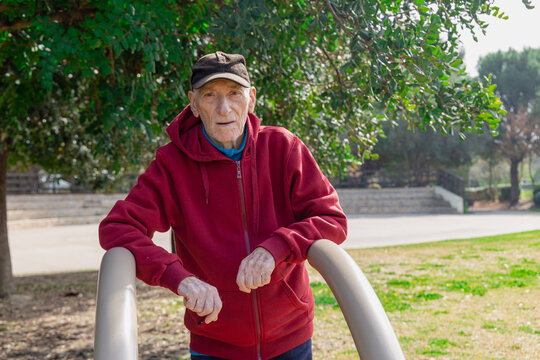 Old man resting on parallel bars in a park
