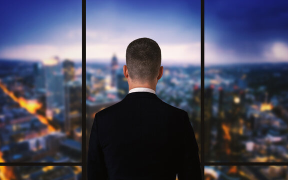 Geschäftsmann steht am Fenster und schaut auf die Skyline