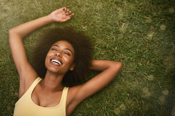 This is the life. Shot of a young woman laughing while relaxing on the grass. - obrazy, fototapety, plakaty
