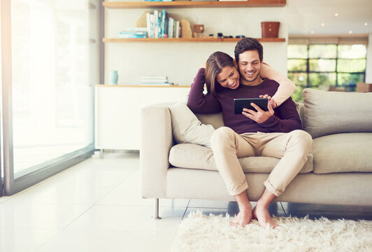 We Are Stuck Together Like Glue. Shot Of A Cheerful Young Couple Using A Digital Tablet While Relaxing On The Sofa At Home.