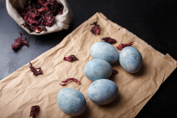 Beautiful DIY painted Easter eggs on craft paper, dry Hibiscus tea in burlap sack. Easter black wooden background