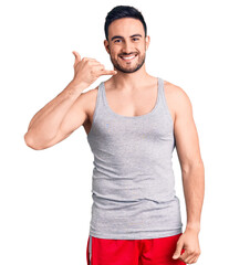 Young handsome man wearing swimwear and sleeveless t-shirt smiling doing phone gesture with hand and fingers like talking on the telephone. communicating concepts.