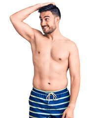 Fototapeta premium Young handsome man wearing swimwear smiling confident touching hair with hand up gesture, posing attractive and fashionable