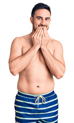 Fototapeta premium Young handsome man wearing swimwear laughing and embarrassed giggle covering mouth with hands, gossip and scandal concept