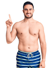 Fototapeta premium Young handsome man wearing swimwear showing and pointing up with finger number one while smiling confident and happy.