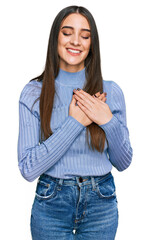 Young beautiful woman wearing casual winter sweater smiling with hands on chest with closed eyes...