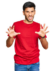 Young handsome man wearing casual red tshirt smiling funny doing claw gesture as cat, aggressive...