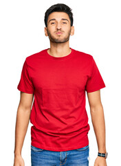 Young handsome man wearing casual red tshirt puffing cheeks with funny face. mouth inflated with air, crazy expression.