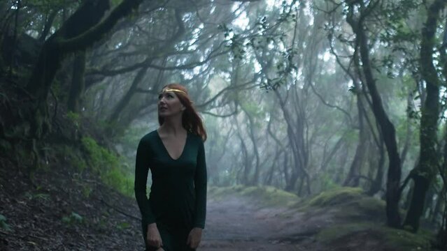 Beautiful woman in an elf costume is walking in a magic green enchanted forest.