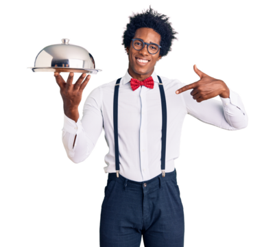 Handsome african american man with afro hair wearing waiter uniform holding silver tray pointing finger to one self smiling happy and proud
