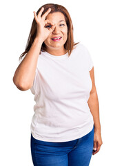 Middle age latin woman wearing casual white tshirt doing ok gesture with hand smiling, eye looking through fingers with happy face.