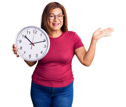Middle age latin woman holding big clock celebrating victory with happy smile and winner expression with raised hands