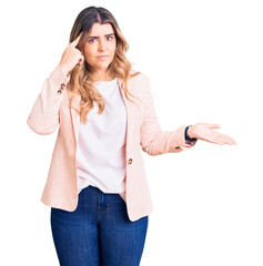 Young caucasian woman wearing business clothes confused and annoyed with open palm showing copy space and pointing finger to forehead. think about it.