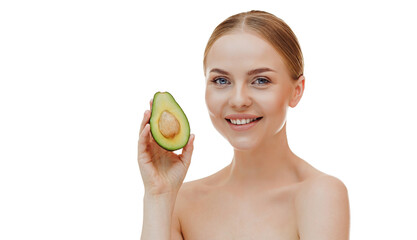 Close up shot of tender blue eyed woman looks directly at camera holds halves of avocado near face chooses healthy nutrition has perfect smooth skin isolated over beige background. beauty concept