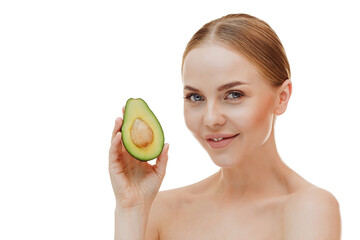 Close up shot of tender blue eyed woman looks directly at camera holds halves of avocado near face chooses healthy nutrition has perfect smooth skin isolated over beige background. beauty concept