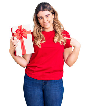 Young caucasian woman holding gift pointing finger to one self smiling happy and proud