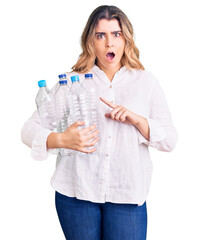 Young caucasian woman holding recycling plastic bottles scared and amazed with open mouth for surprise, disbelief face