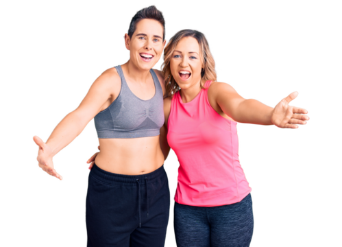 Couple of women wearing sportswear looking at the camera smiling with open arms for hug. cheerful expression embracing happiness.