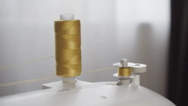 The process of winding thread on the bobbin of a modern sewing machine. Close-up of a spool with yellow thread. Professional sewing equipment detail, working tool