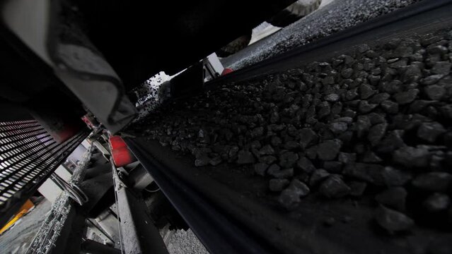 Gravel ore on moving conveyor belt at rock mining quarry close view. Crushing system operates with extracted materials